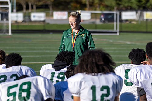 Wilde Lake High School JV Football Coach Chantal Thacker standing with players on the team kneeling in front of her